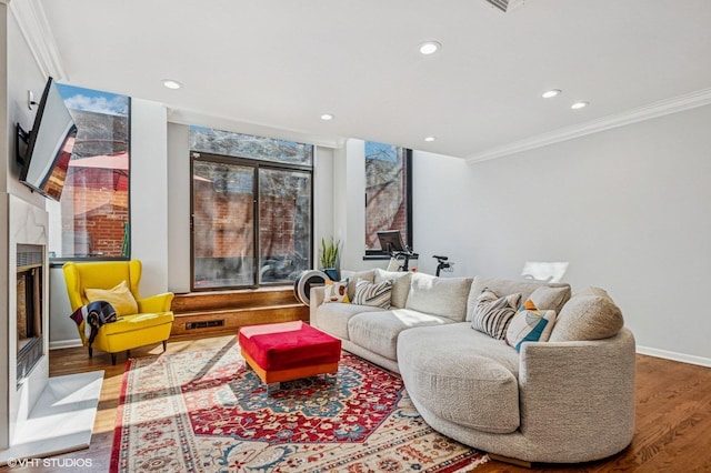 living area with crown molding, baseboards, recessed lighting, a fireplace, and wood finished floors