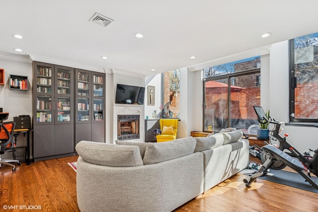 living area with wood finished floors, visible vents, recessed lighting, a fireplace, and ornamental molding