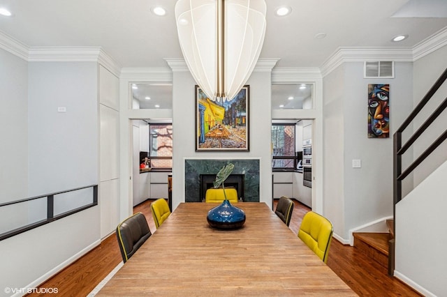 dining space featuring visible vents, wood finished floors, a fireplace, crown molding, and stairs