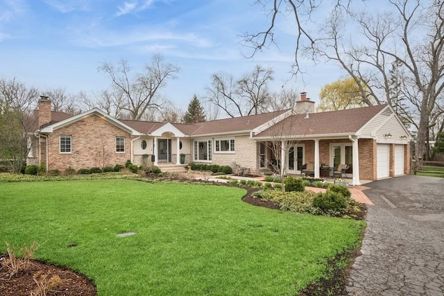 single story home featuring a chimney, brick siding, aphalt driveway, and a front lawn