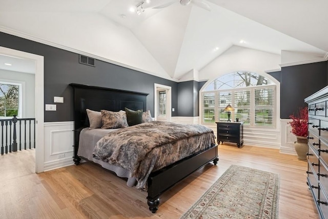 bedroom with light wood finished floors, a wainscoted wall, visible vents, and vaulted ceiling