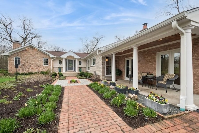 rear view of house featuring a chimney, brick siding, and french doors