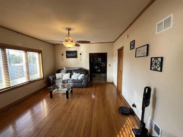 living room featuring wood-type flooring, visible vents, a ceiling fan, and ornamental molding