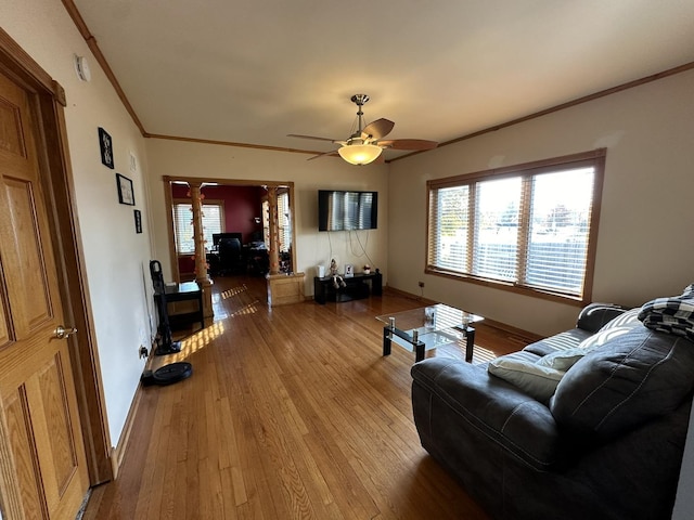 living area featuring ceiling fan, baseboards, ornamental molding, light wood-type flooring, and ornate columns