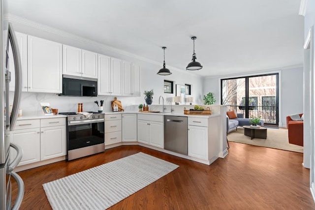 kitchen featuring ornamental molding, open floor plan, a peninsula, stainless steel appliances, and a sink