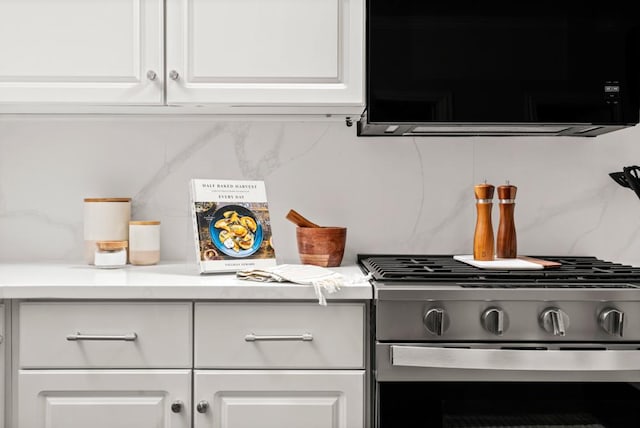 details with gas stove, white cabinets, light countertops, and decorative backsplash