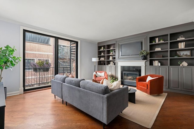 living area with built in features, a premium fireplace, ornamental molding, wood finished floors, and baseboards