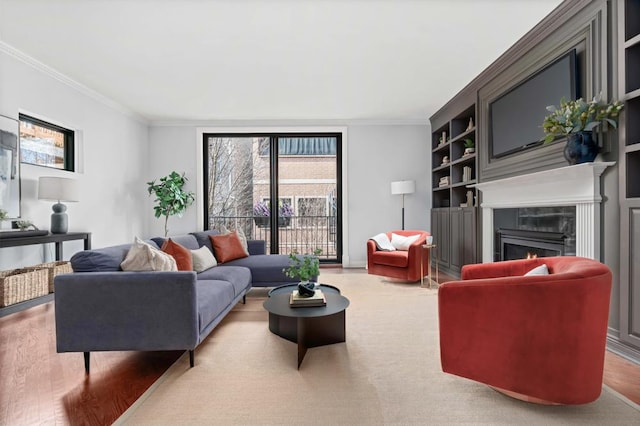 living room with built in shelves, a fireplace, wood finished floors, baseboards, and crown molding