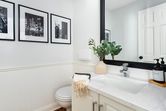 half bath featuring a wainscoted wall, vanity, and toilet