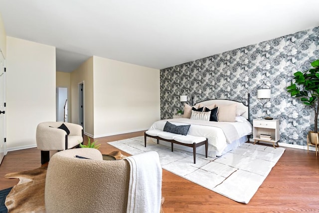 bedroom with an accent wall, wood finished floors, baseboards, and wallpapered walls