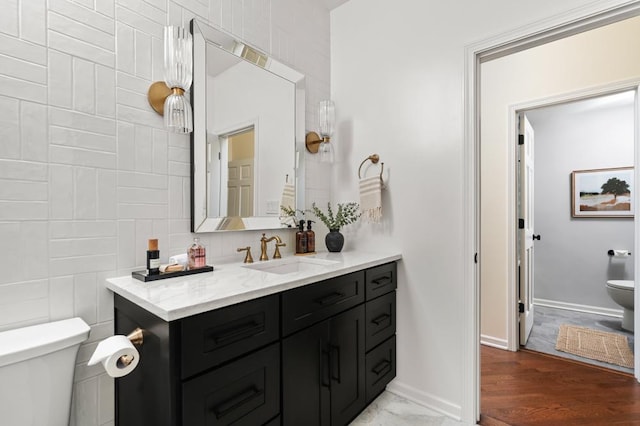 bathroom featuring toilet, baseboards, tile walls, and vanity