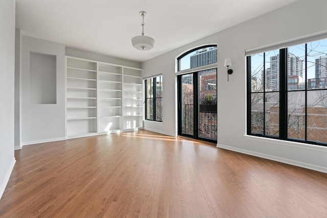 unfurnished room with built in shelves, a healthy amount of sunlight, baseboards, and wood finished floors