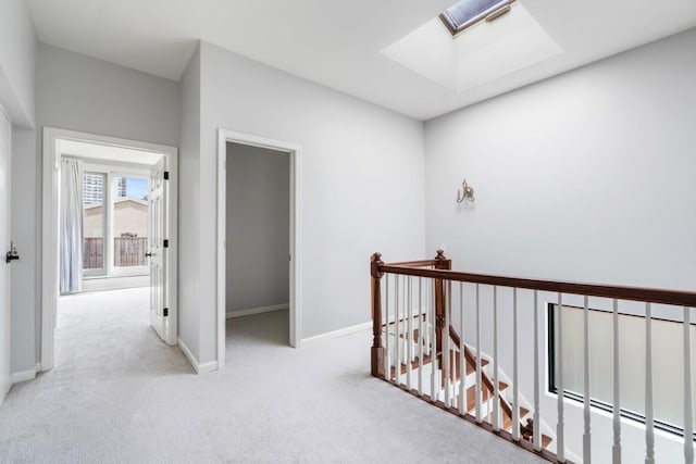 corridor featuring a skylight, carpet, baseboards, and an upstairs landing