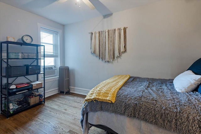 bedroom featuring baseboards, a ceiling fan, radiator, wood finished floors, and cooling unit