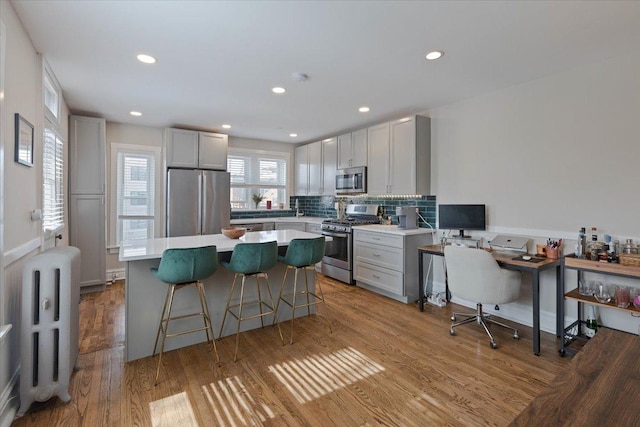 kitchen with a center island, radiator, backsplash, appliances with stainless steel finishes, and light wood-type flooring