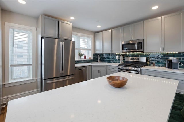 kitchen with tasteful backsplash, stainless steel appliances, gray cabinetry, a sink, and recessed lighting