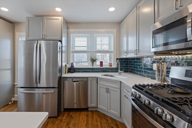 kitchen featuring decorative backsplash, dark wood-style floors, appliances with stainless steel finishes, light countertops, and a sink