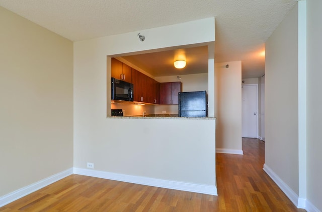 kitchen featuring baseboards, a textured ceiling, black appliances, and wood finished floors