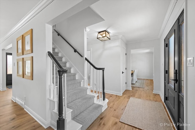 foyer entrance featuring baseboards, wood finished floors, stairs, and crown molding