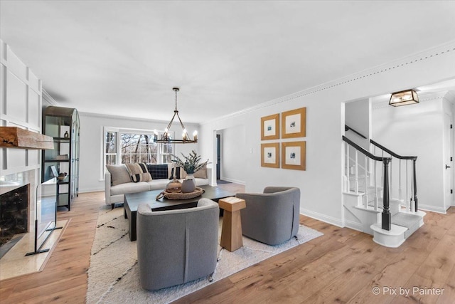 living room with stairway, crown molding, light wood-style floors, a notable chandelier, and a high end fireplace