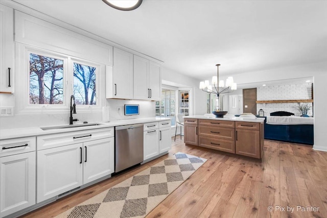 kitchen featuring light wood-style flooring, light countertops, stainless steel dishwasher, white cabinetry, and a sink