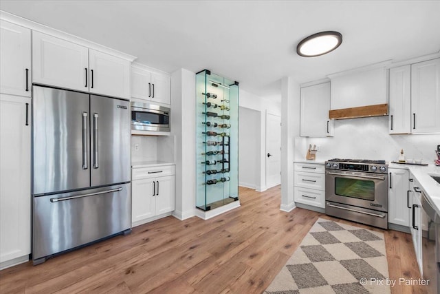 kitchen featuring high end appliances, white cabinets, light countertops, and light wood finished floors