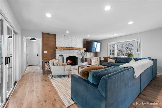 living area featuring baseboards, recessed lighting, a brick fireplace, and light wood-style floors