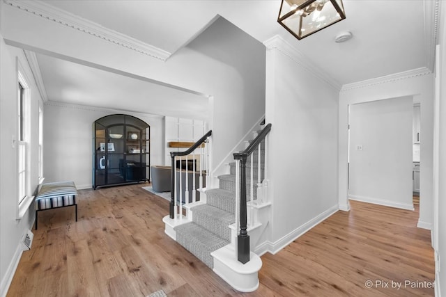 entryway with arched walkways, crown molding, stairway, wood finished floors, and baseboards