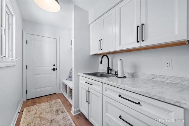 kitchen featuring dark wood-style floors, white cabinets, a sink, and light stone counters