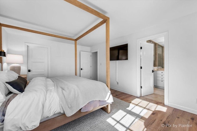 bedroom with light wood-type flooring, baseboards, and connected bathroom