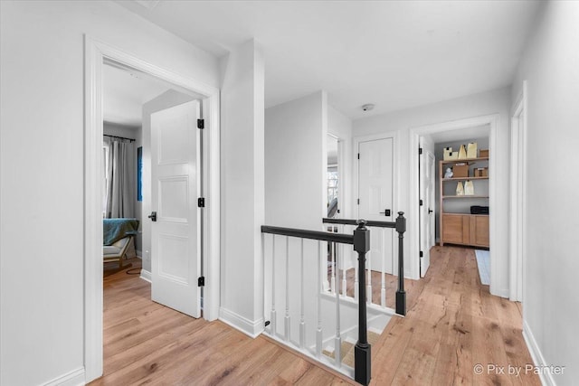 hall with baseboards, an upstairs landing, and light wood-style floors