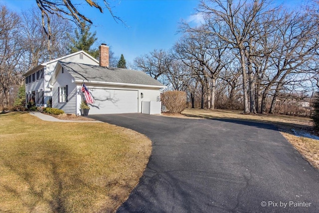 view of side of home featuring aphalt driveway, a garage, a shingled roof, a lawn, and a chimney