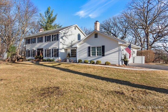 colonial home with aphalt driveway, a chimney, and a front lawn