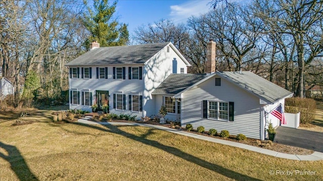 colonial-style house with a garage, aphalt driveway, a chimney, and a front lawn