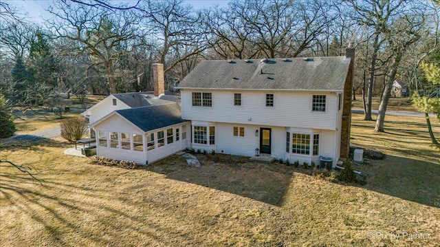 back of property with a sunroom, roof with shingles, a chimney, and a yard