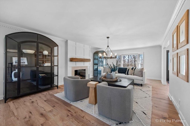 living area featuring light wood finished floors, baseboards, crown molding, a fireplace, and a notable chandelier