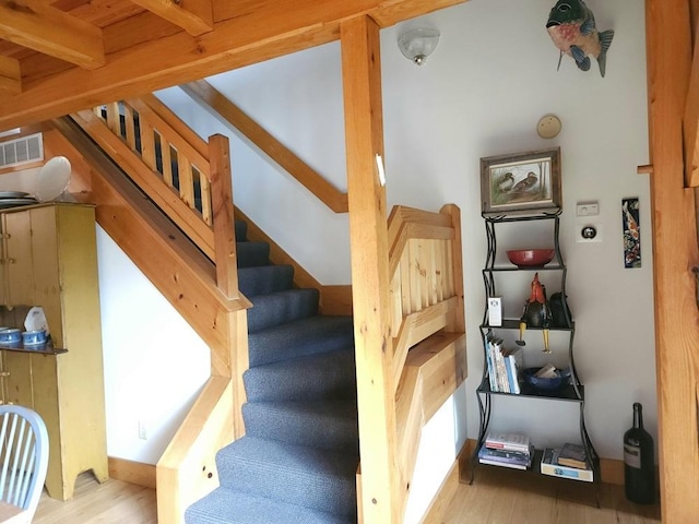 stairs with beam ceiling, visible vents, and wood finished floors