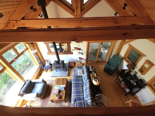 living room with high vaulted ceiling, a wood stove, beam ceiling, and wood finished floors