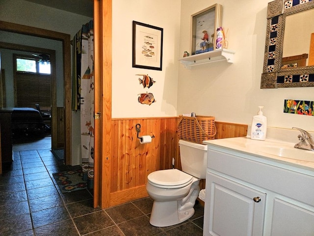 full bath featuring a wainscoted wall, wood walls, vanity, and toilet