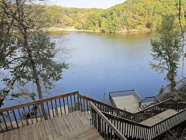 dock area featuring a water view, stairway, and a wooded view