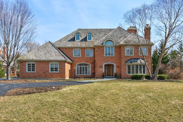 view of front of property featuring a front yard, a chimney, and brick siding