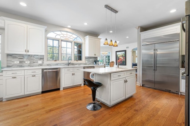 kitchen featuring light wood finished floors, appliances with stainless steel finishes, light countertops, white cabinetry, and backsplash