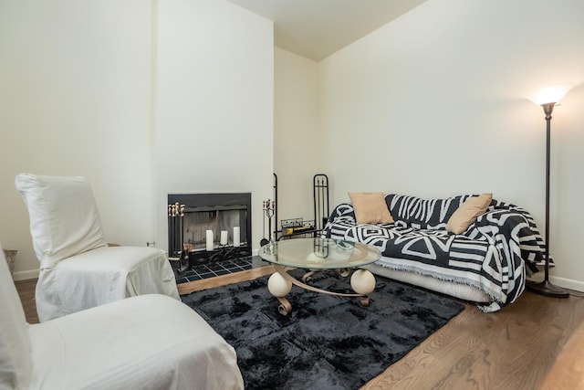 living area featuring a fireplace with flush hearth, wood finished floors, and baseboards