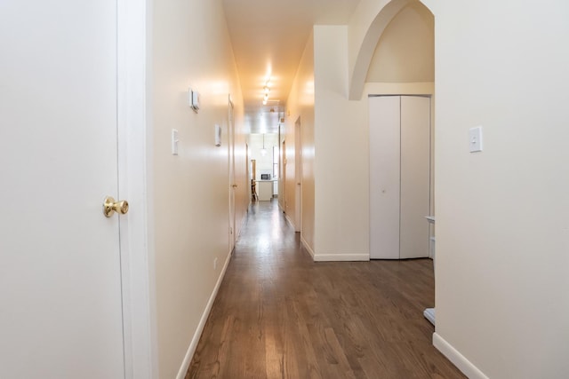 hall with baseboards, arched walkways, and wood finished floors