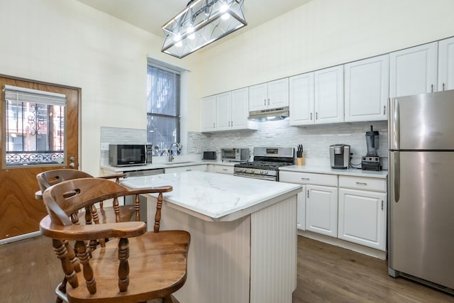 kitchen with tasteful backsplash, white cabinets, a kitchen island, appliances with stainless steel finishes, and under cabinet range hood