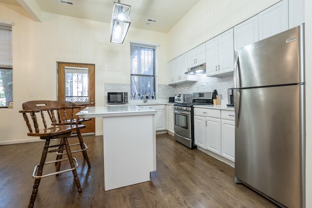 kitchen with under cabinet range hood, white cabinetry, light countertops, appliances with stainless steel finishes, and tasteful backsplash