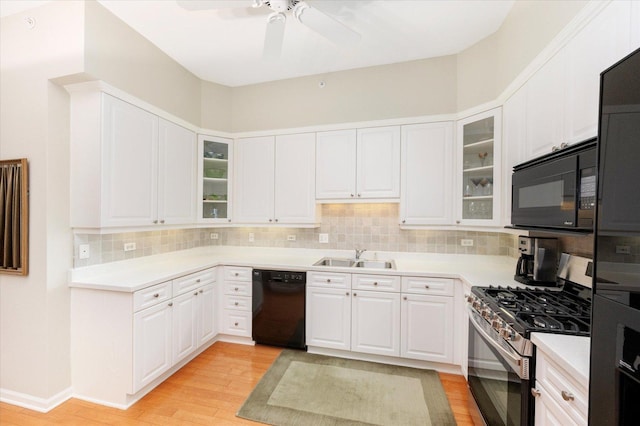 kitchen featuring light wood-style flooring, a sink, decorative backsplash, black appliances, and white cabinetry