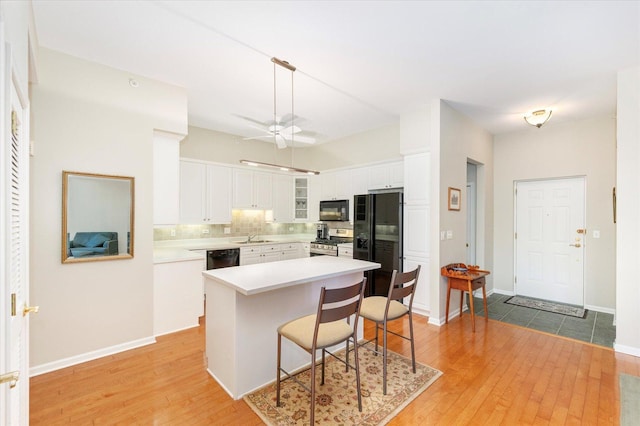 kitchen with tasteful backsplash, black appliances, white cabinets, and light wood finished floors