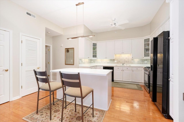 kitchen with visible vents, a kitchen breakfast bar, black appliances, and light wood-style flooring