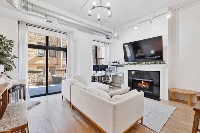 living area featuring a fireplace with flush hearth, rail lighting, hardwood / wood-style floors, and an inviting chandelier